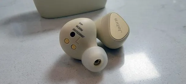 The Jabra Elite 5 earbuds in front of their charging case. Golden color, sort of reminds one of C3P0